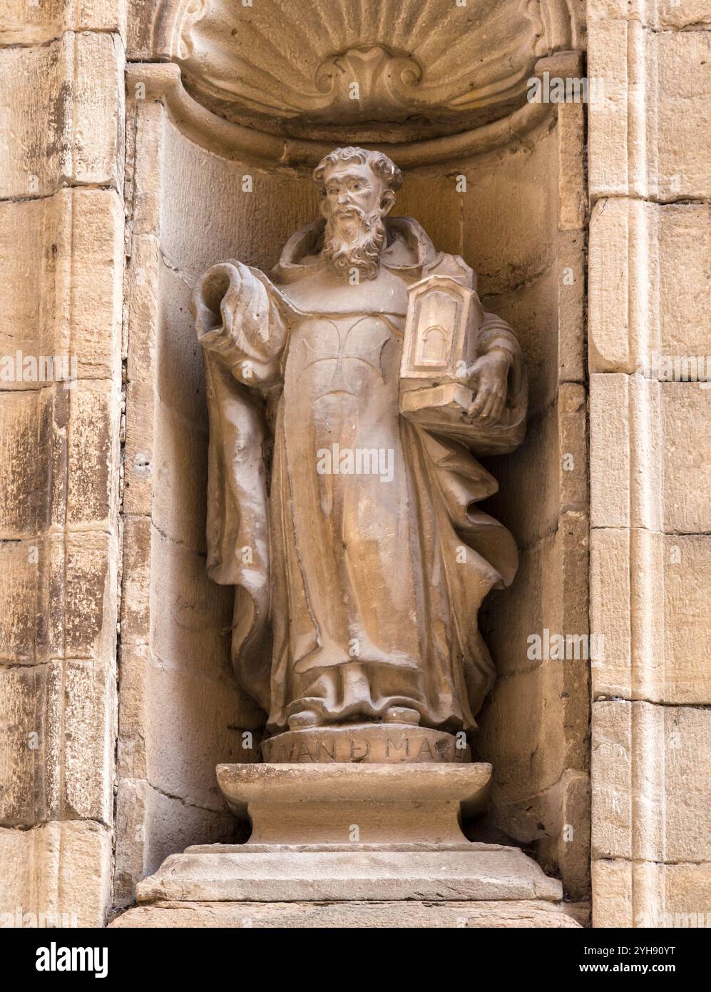 In einer Nische steht eine geschnitzte Figur, die ein Buch hält und komplizierte architektonische Details zeigt. Stockfoto