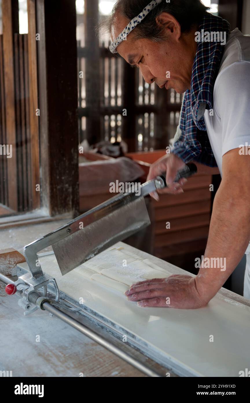 Der Koch schneidet den Teig von Hand in winzige Streifen, um Soba Buchweizennudeln für Suppen zu machen. Stockfoto