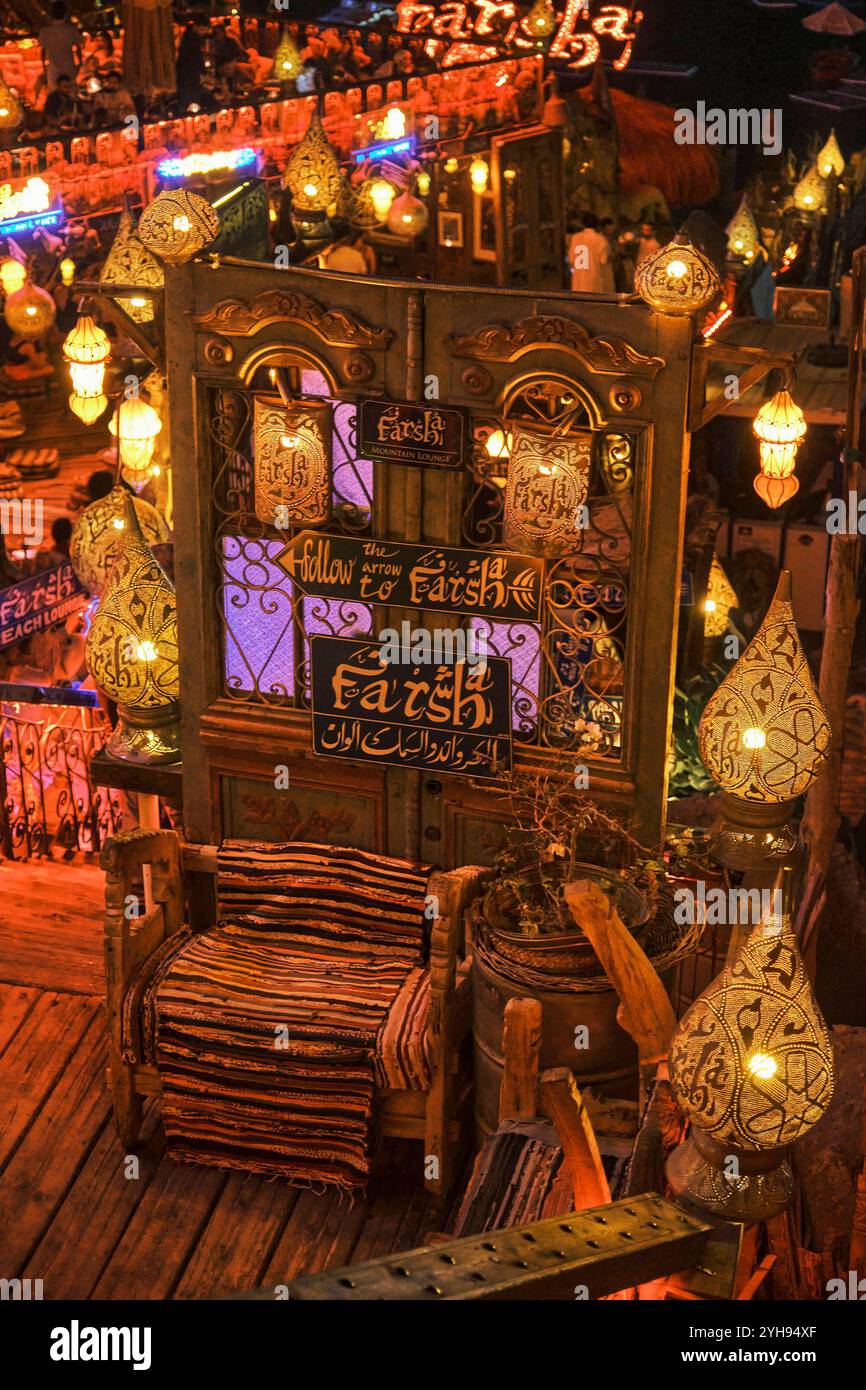 Sharm El Sheikh, Ägypten - 30. April 2024: Rustikales Wohnzimmer mit hellem gewebtem Teppich auf Holzstuhl und Vintage-Tür. Leuchtende Laternen im orientalischen Stil, ecl Stockfoto