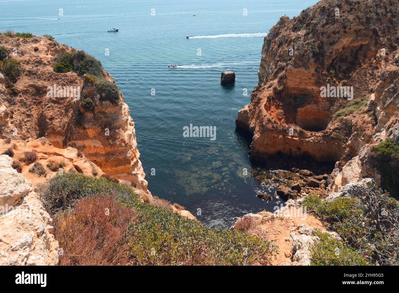 Boote fahren durch klares Wasser, das von hohen Klippen eingerahmt wird, in Ponta da Piedade Stockfoto