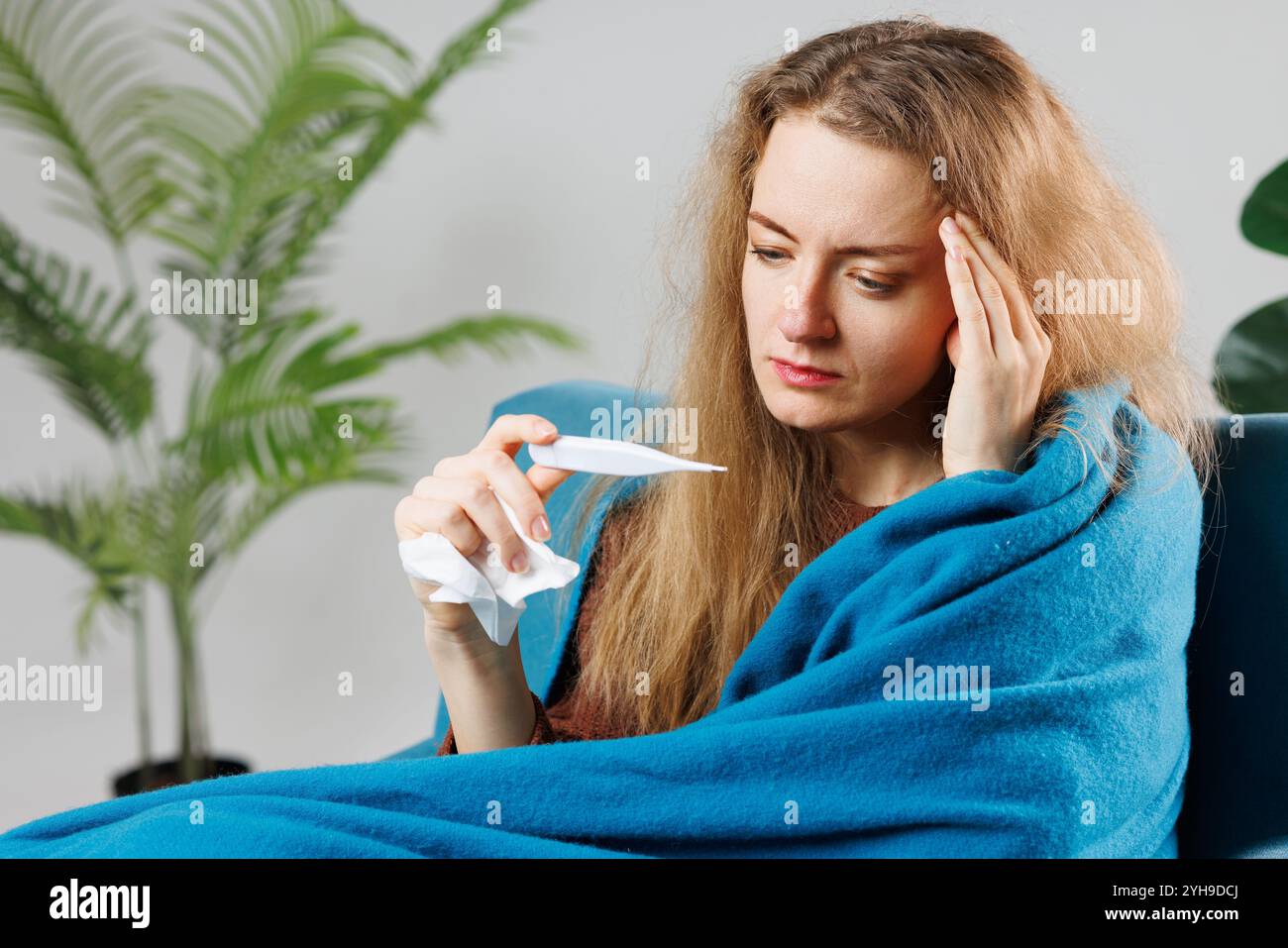 Ein krankes Mädchen mit einer Erkältung oder Grippe in eine blaue Decke gewickelt misst ihre Temperatur zu Hause, Symptome, Behandlung von Viruserkrankungen Stockfoto