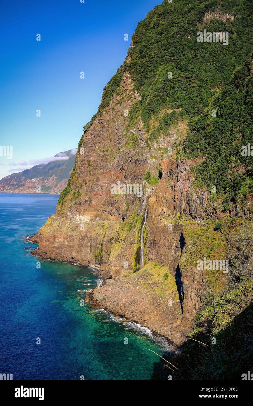 Ein atemberaubendes Landschaftsbild, das eine zerklüftete Klippe zeigt, die in den Ozean stürzt. Das helle Sonnenlicht beleuchtet das üppige Grün und das felsige Gelände. Stockfoto