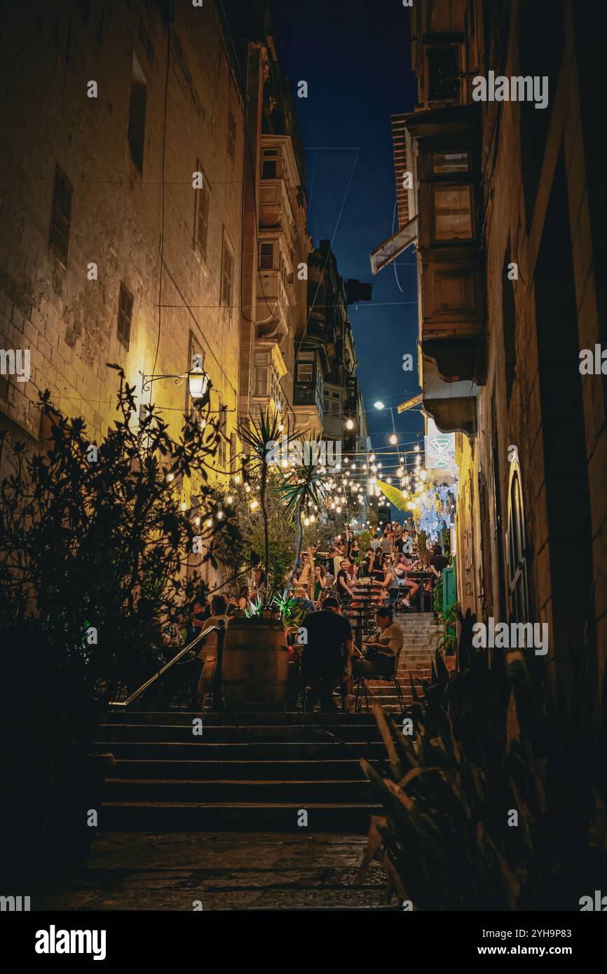 Eine lebhafte Abendszene in einer engen Straße mit Speisen im Freien und Lichterketten. Die Leute genießen ihre Zeit auf der Treppe. Stockfoto