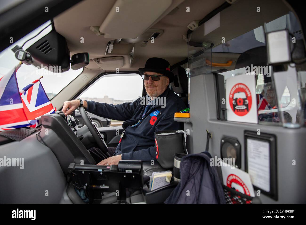 London, Großbritannien. November 2024. Ein Londoner Taxifahrer sitzt vor seinem Taxi. Poppy Cabs wurde vor 15 Jahren von Londoner Taxifahrern gegründet und bietet Militärveteranen kostenlose Fahrten an, die am jährlichen Gedenktag-Service im Cenotaph in Westminster, London, teilnehmen. Inspiriert vom Poppy Appeal der Royal British Legion, wo rote Mohnabzeichen gegen Spenden ausgetauscht werden, organisieren sich diese engagierten Taxifahrer im Rahmen der „Poppy Cabs“-Initiative. Jedes Jahr bieten Fahrer kostenlose Fahrten zu Veteranen von den großen Bahnhöfen in ganz London an, um sicherzustellen, dass die Fahrten nicht zu kurz kommen Stockfoto