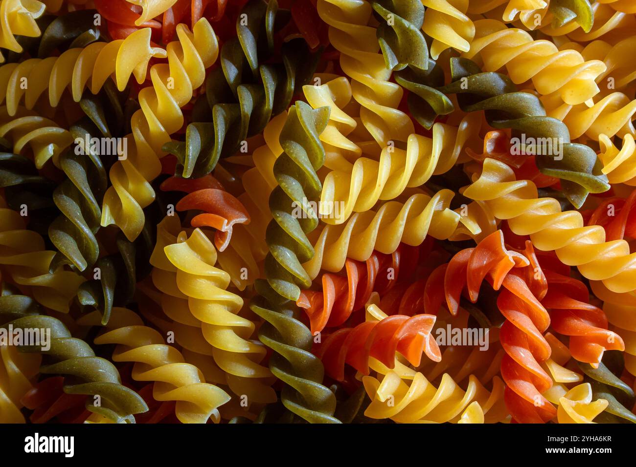 Ungekochte Fusilli Pasta in leuchtenden Farben: Eine faszinierende kulinarische Leinwand aus bunten Spiralen, die einen lebendigen und strukturierten Hintergrund für Gourmet-Kochen schafft. Farbige Trockene Pasta. Rohe Makkaroni Stockfoto