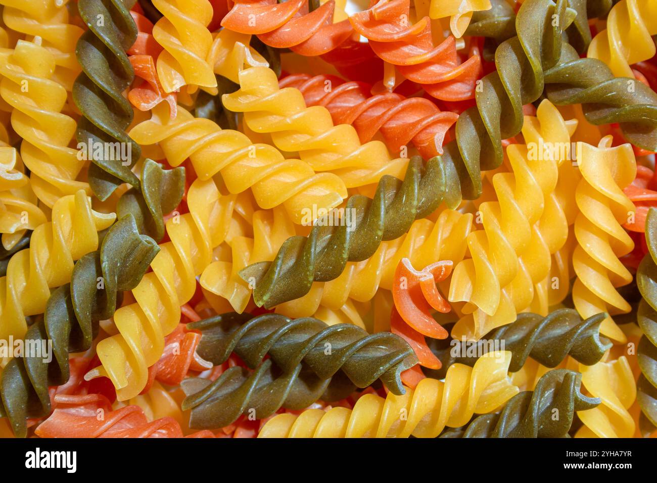 Ungekochte Fusilli Pasta in leuchtenden Farben: Eine faszinierende kulinarische Leinwand aus bunten Spiralen, die einen lebendigen und strukturierten Hintergrund für Gourmet-Kochen schafft. Farbige Trockene Pasta. Rohe Makkaroni Stockfoto