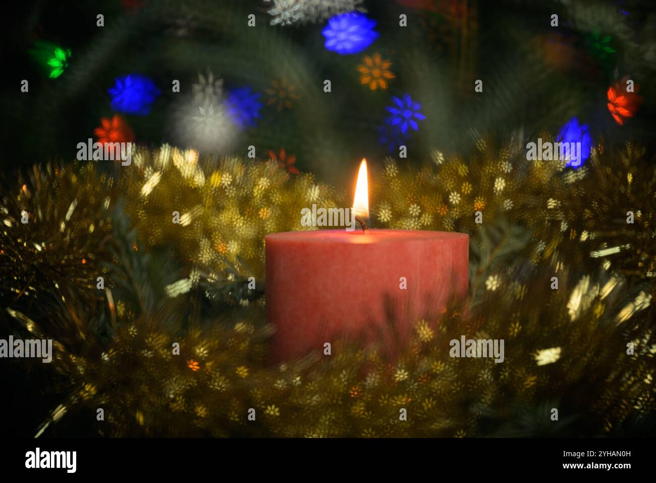 Rote Weihnachtskerze brennt, umgeben von einem Kranz und bunten Schneeflocken-Bokeh-Highlights Stockfoto