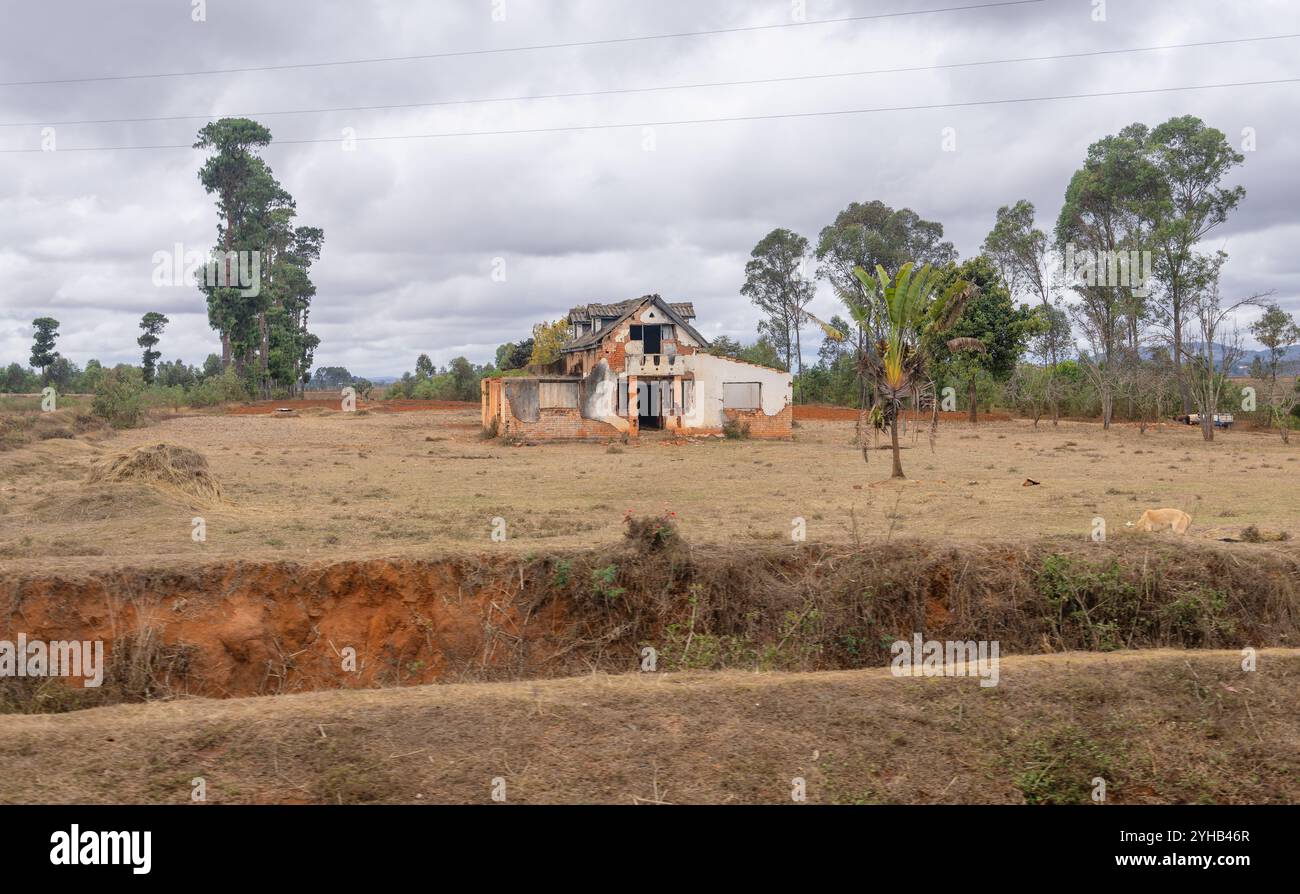 Ein verlassenes Haus aus rotem Backstein steht allein mitten auf einem Feld. Die Straße, die zum Park führt, ist von dieser rustikalen Landschaft gesäumt. Isalo National Par Stockfoto
