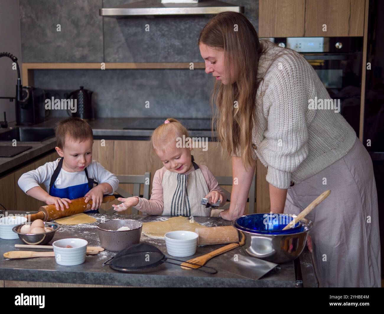 Mutter und ihre Kinder bereiten in einer modernen Küche gerne Keksenteig zu, während sie über das Backen kleben. Die Familie genießt eine gute Zeit zusammen, lernen und Stockfoto