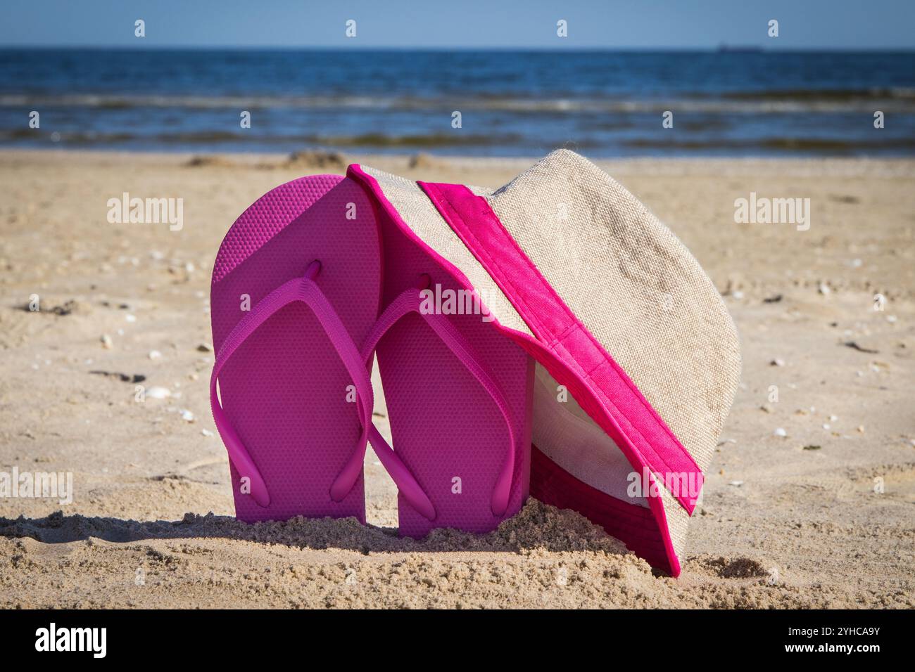 Strohhut und pinkfarbene Hausschuhe am Strand. Zubehör zum Entspannen im Sommer Stockfoto