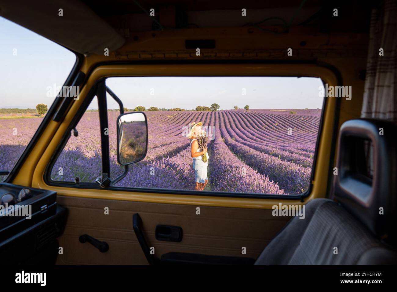 Junge blonde Frau genießt die Aussicht in ihrem gelben Retro-Wohnwagen bei Sonnenaufgang in Valensole Lavendelfeldern in der Provence, Südfrankreich Stockfoto