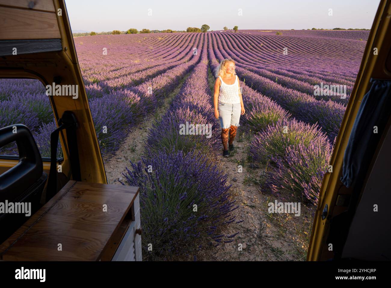 Junge blonde Frau genießt die Aussicht in ihrem gelben Retro-Wohnwagen bei Sonnenaufgang in Valensole Lavendelfeldern in der Provence, Südfrankreich Stockfoto