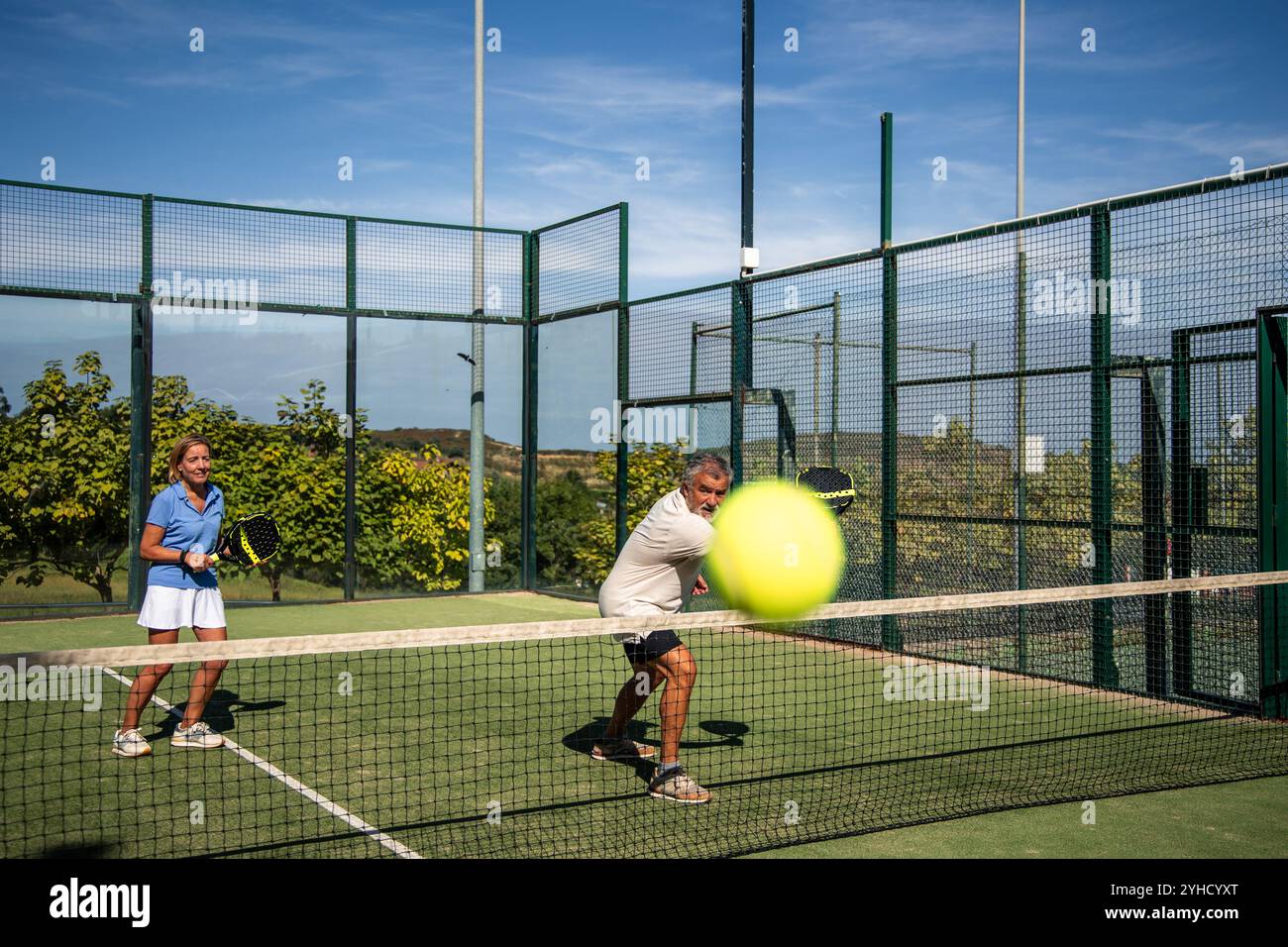 Das Seniorenpaar auf dem Padel-Platz gibt eine Aufnahme direkt in die Kamera zurück und zeigt dabei ihren Fokus und ihre Teamarbeit. Ihre synchronisierten Bewegungen spiegeln sich wider Stockfoto