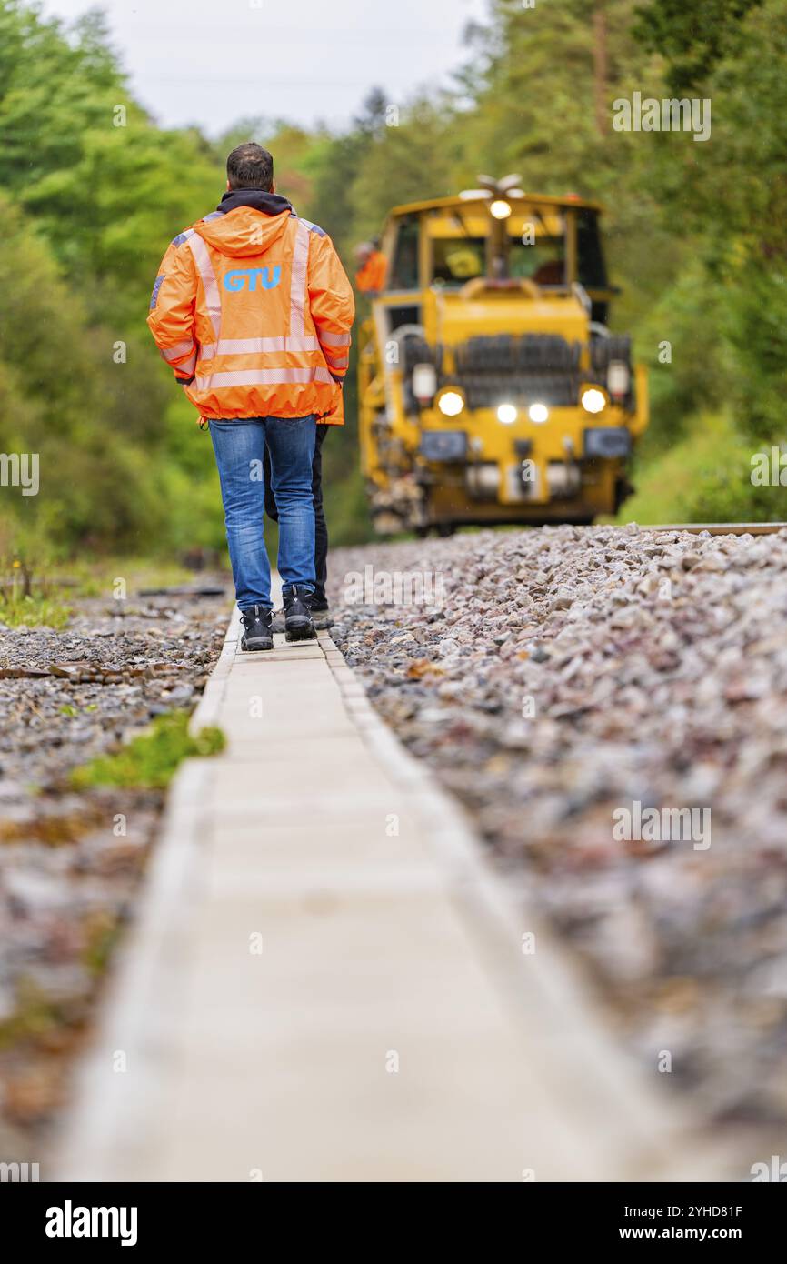 Ein Mann in orangefarbener Jacke geht auf einer Bahnstrecke entlang, ein gelber Traktor folgt, Gleisbau Hermann Hesse Bahn, Bezirk Calw, Schwarzwald, Stockfoto