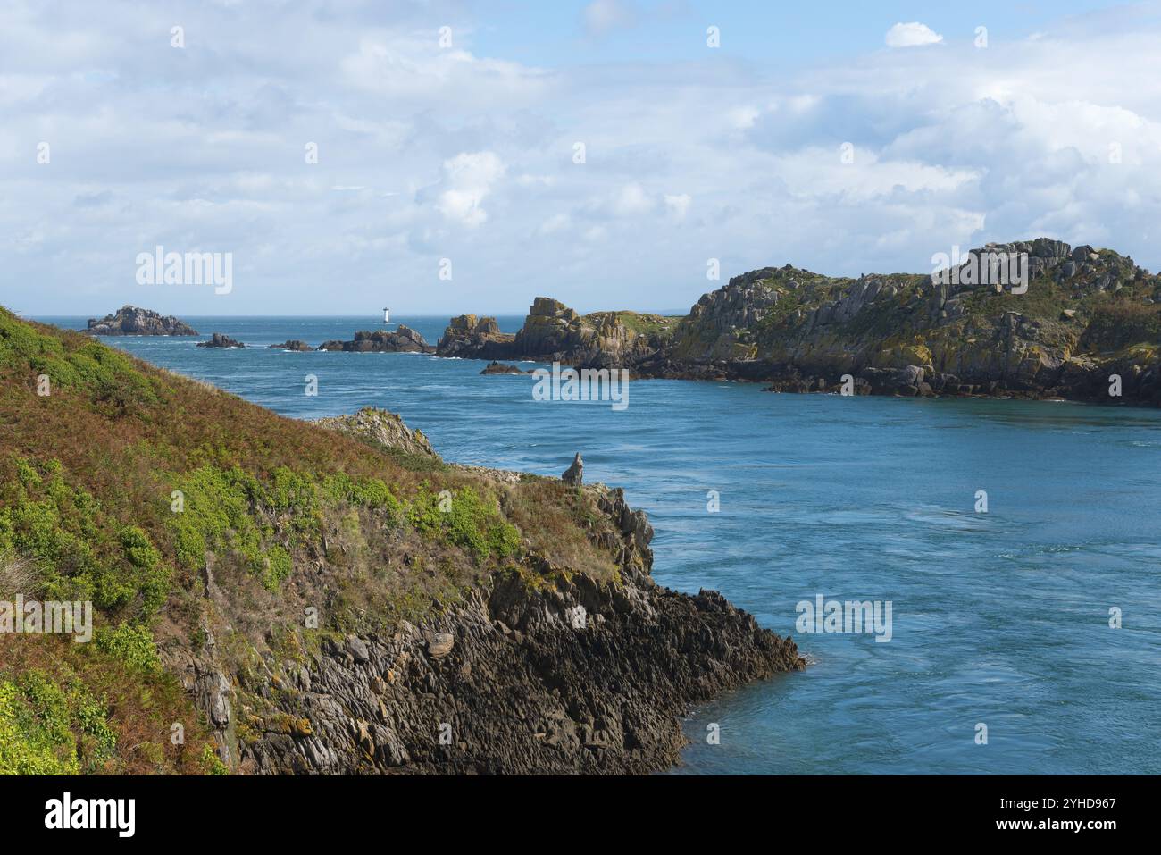 Küstenlandschaft mit rauen Felsen und blauem Meer unter bewölktem Himmel, Pointe du Grouin, Naturschutzgebiet Insel Ile des Landes und Leuchtturm La Pierre de Stockfoto