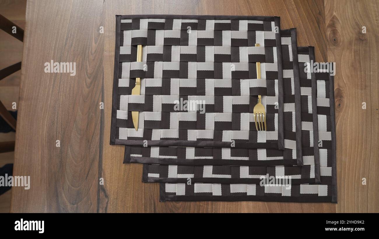 Stapel karierter Tischsets auf Holztisch mit goldenem Besteck ordentlich angeordnet Stockfoto