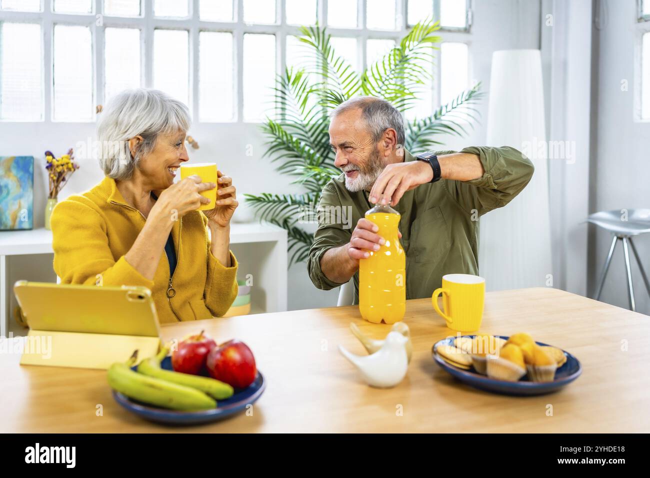 Seniorenpaar genießen gesundes Frühstück zu Hause mit Tablet und sprechen zusammen Stockfoto