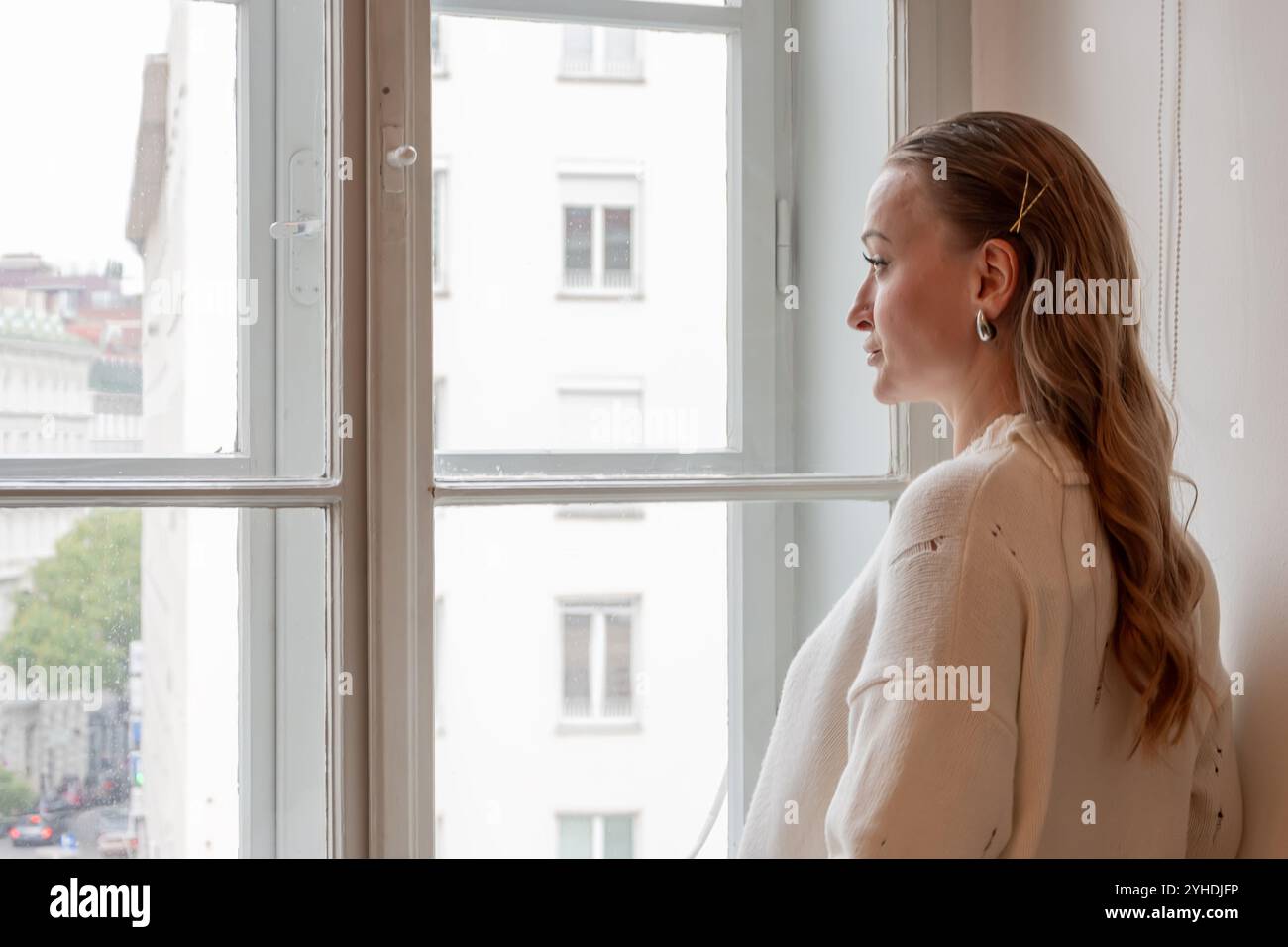 Emotionales Porträt einer Frau an einem Fenster mit Blick auf die Altstadt. Stockfoto