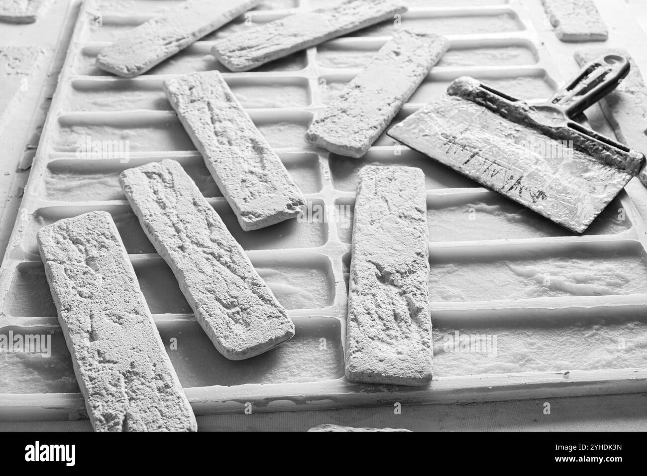 Fertige Dekorziegel, Spachtel und Silikonform zum Gießen von Baugips. Schwarzweißfoto Stockfoto