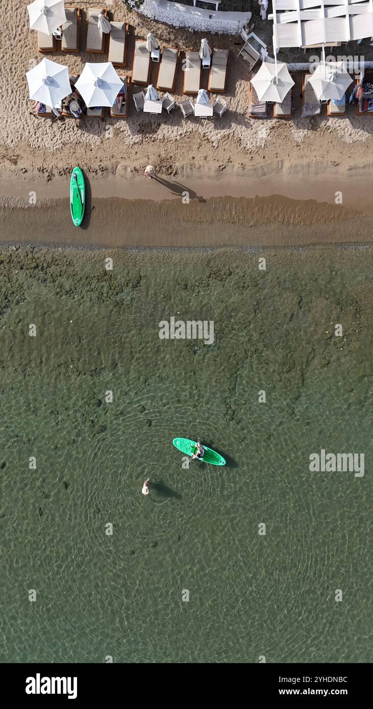 Blick aus der Vogelperspektive auf den unberührten Strand mit weißen Sonnenschirmen und Sonnenliegen, im Kontrast zu hellgrünen Paddleboards und klarem türkisfarbenem Wasser Stockfoto