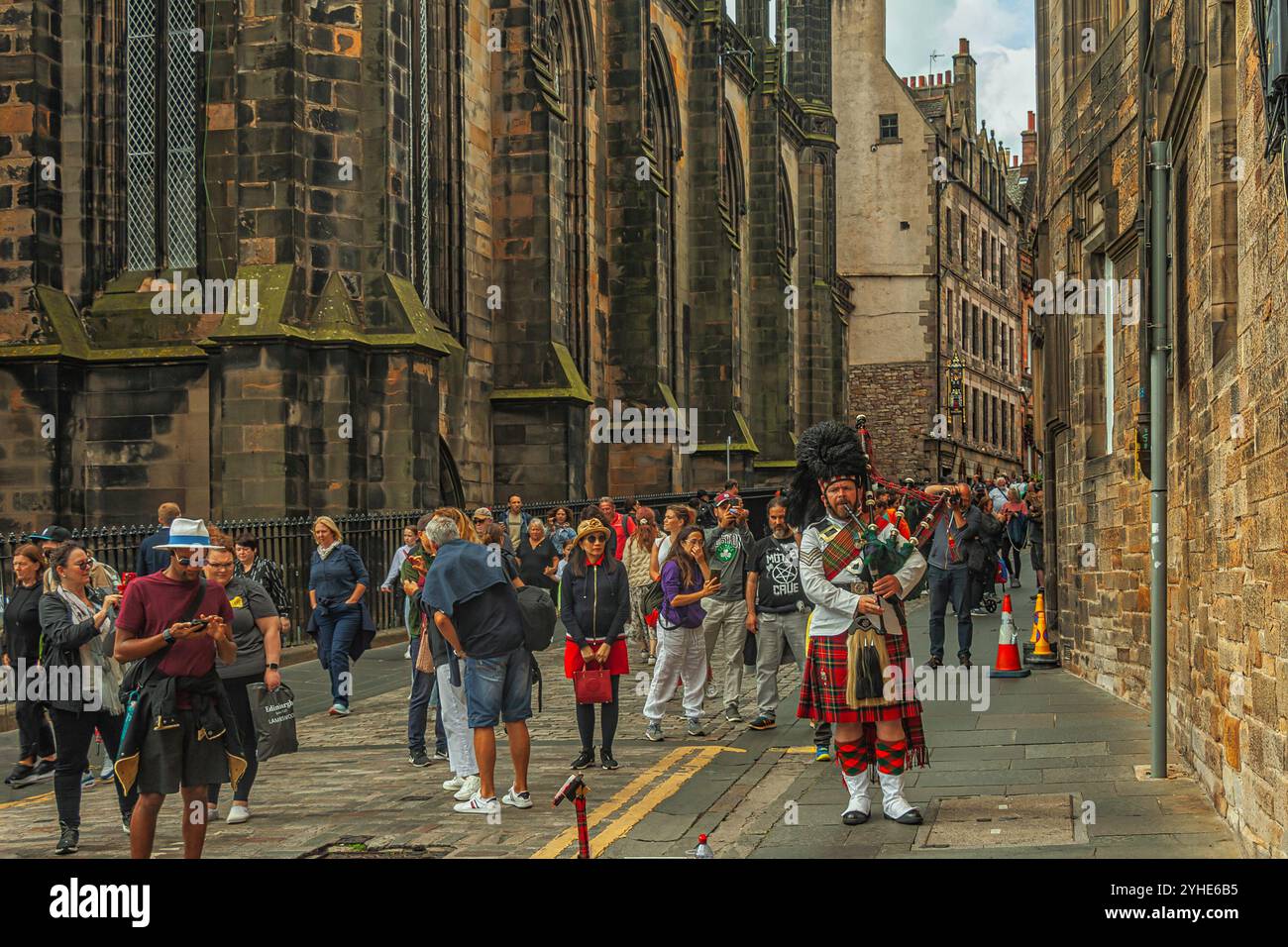 Touristen schlendern entlang des Lawnmarket in Edinburghs Altstadt. Ein Schauspieler in traditioneller schottischer Kleidung spielt den Dudelsack. Schottland Stockfoto