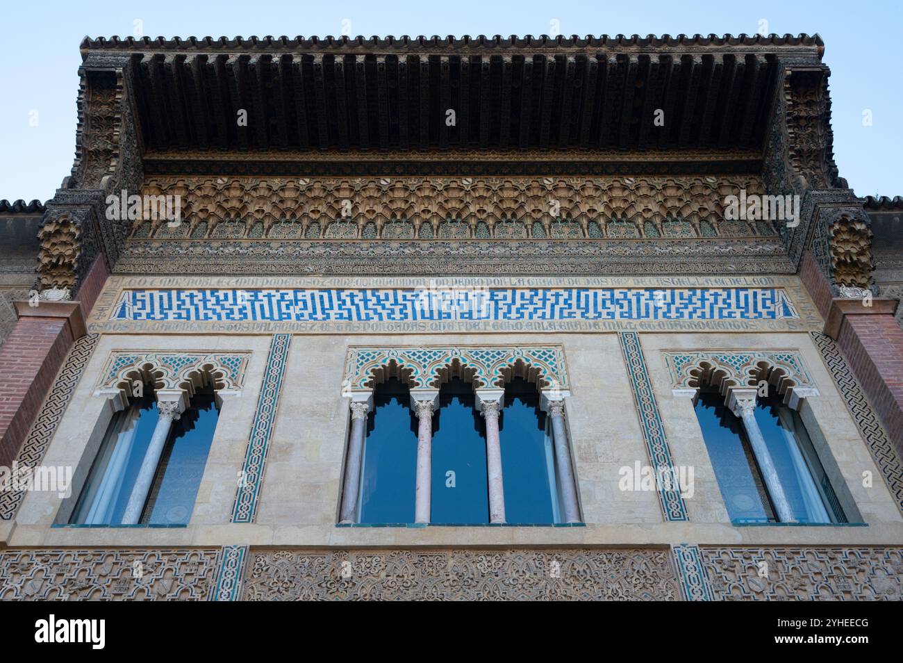 Die Spitze eines wunderschönen historischen Gebäudes in Sevilla, geschmückt mit bunten Fliesen, komplizierten Holzarbeiten und drei eleganten Fenstern, die von Säulen eingerahmt sind Stockfoto