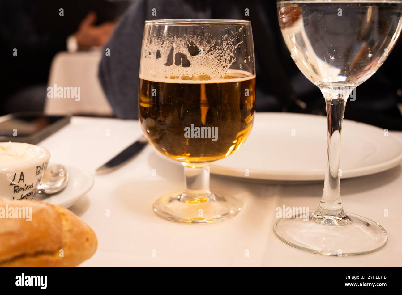 Ein erfrischendes Glas Bier liegt auf einem Esstisch vor einem leeren Teller Stockfoto