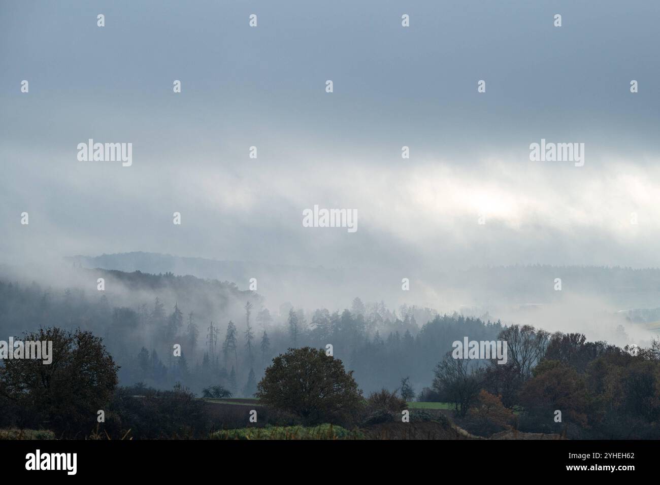 Sonnenstrahlen durchbrechen die Nebelwolken 11.11.24, Selters im Taunus: Symbolfoto, Illustrationsbild, Symbolbild, Illustrationsfoto, Alltagsszene Sonnenstrahlen durchbrechen die Nebelwolken ein dramatisches Naturschauspiel, bei dem Sonnenstrahlen durch dichte, tiefhängende Wolken brechen und die neblige Herbstlandschaft in sanftes Licht tauchen. Die Hügel und Wälder wirken geheimnisvoll und stimmungsvoll, während der Himmel sich in dramatischen Grautönen zeigt. Selters im Taunus Hessen *** Sonnenstrahlen brechen durch die Nebelwolken 11 11 24, Selters im Taunus Symbolfoto, Illustration pi Stockfoto