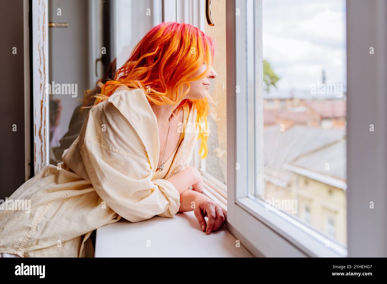Nachdenkliche Frau mit leuchtendem Haar, die aus dem Fenster blickt Stockfoto