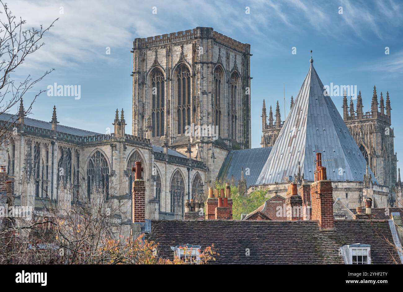 Die Türme des York Minster, von den Dächern einiger historischer Gebäude aus gesehen. Im Vordergrund stehen Bäume und ein Himmel mit Wolken. Stockfoto