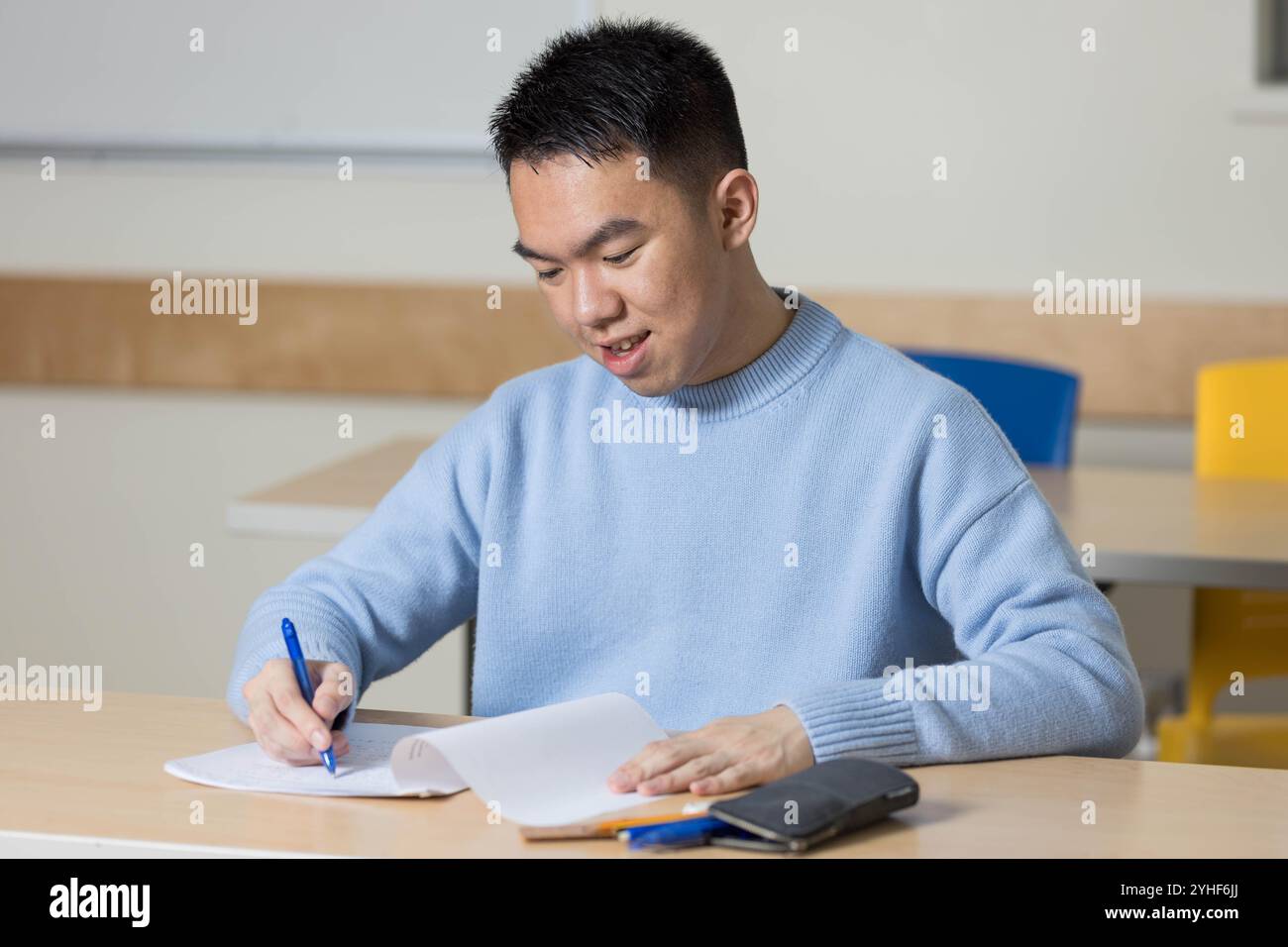 Ein junger Student konzentriert sich darauf, seine Prüfung in einem Schulklassen mit seinem Stift zu schreiben Stockfoto