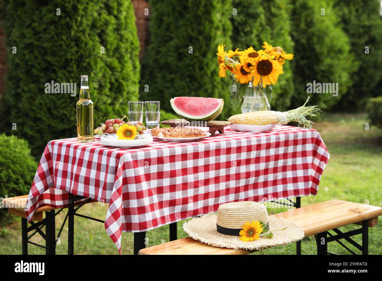 Frisches Obst, Kuchen, Flasche Getränk und Vase mit Sonnenblumen auf dem Tisch im Garten Stockfoto