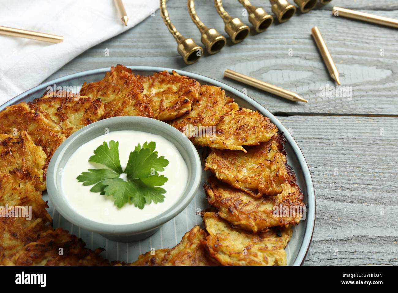 Leckere Kartoffelpfannkuchen, Menora und Kerzen auf grauem Holztisch, Nahaufnahme. Hanukkah festliches Essen Stockfoto