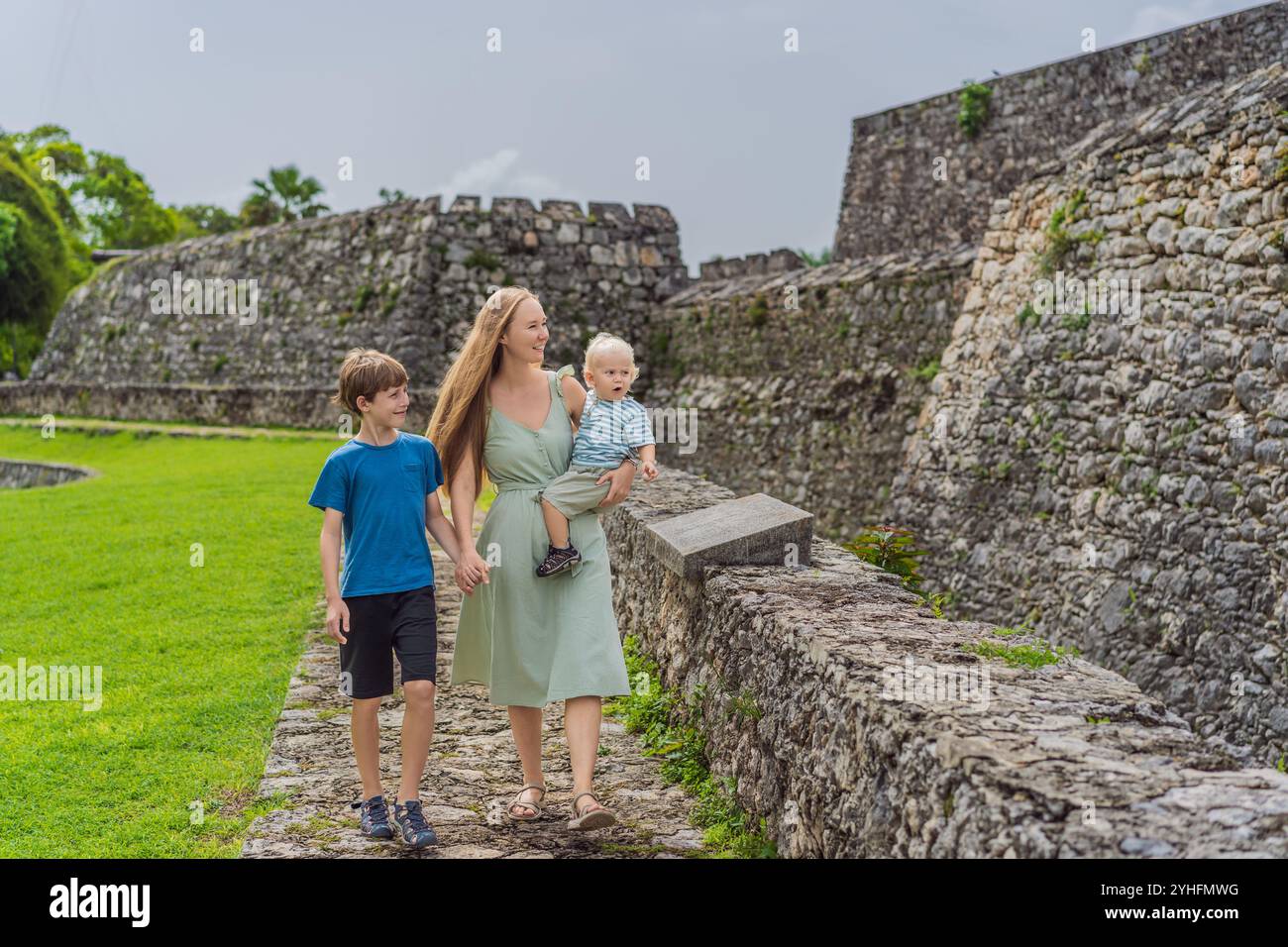 Mutter mit ihrem Kleinkind und ihren Söhnen im Teenageralter erforscht Fuerte de San Felipe de Bacalar. Familienreisen, kulturelles Erbe und historisches Abenteuerkonzept Stockfoto