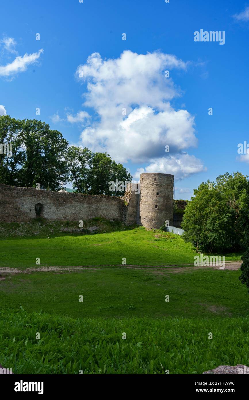 Eine mittelalterliche Steinfestung mit einem hohen runden Turm und weitläufigen Mauern vor einem klaren blauen Himmel. Das Gebäude steht auf einer grasbewachsenen Fläche und erinnert an Hallo Stockfoto