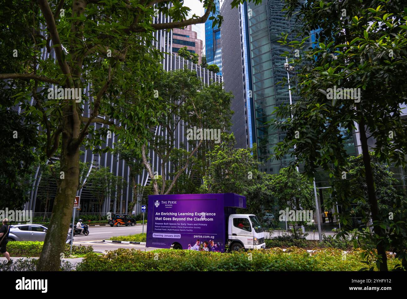 Ein Van mit Werbung für die Perse-Schule, der durch das Finanzviertel von Singapur fährt, eingerahmt von Bäumen gegen die Wolkenkratzer. Stockfoto