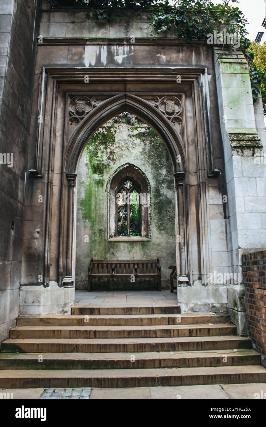 Ein alter, verwitterter Steinbogen mit einer Bank darunter und einem teilweise bewachsenen Fenster, das die Schönheit verlassener Architektur zeigt. Stockfoto