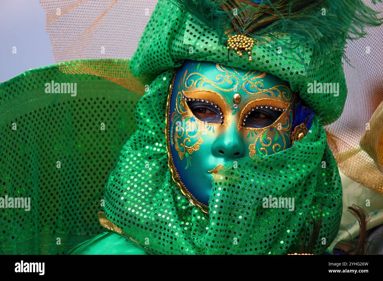 Eine Nahaufnahme einer Person, die ein leuchtend grünes venezianisches Karnevalskostüm trägt, mit einer atemberaubenden grünen Maske, die mit komplizierten Goldmotiven verziert ist. Stockfoto