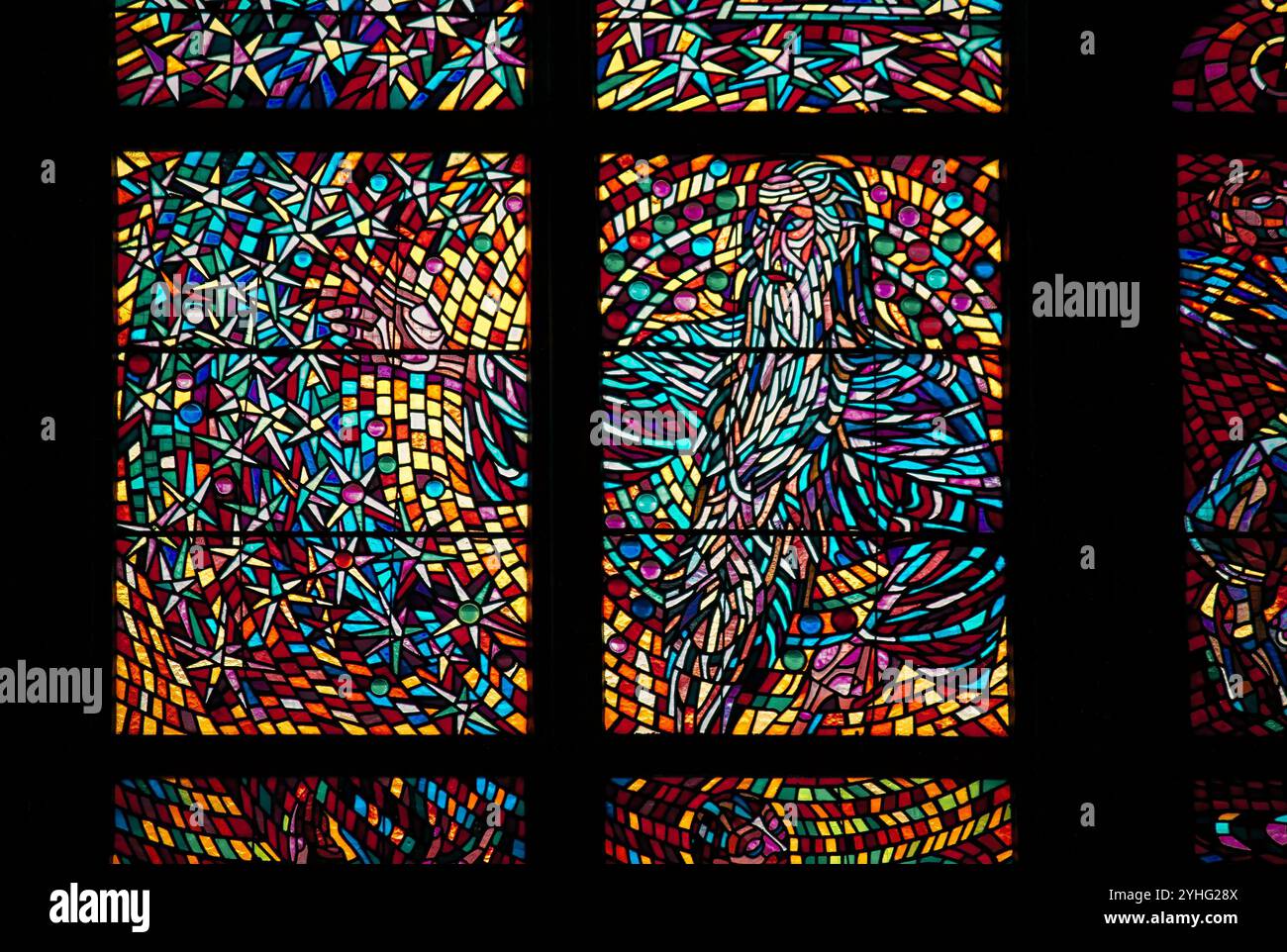Eine Nahaufnahme eines bunten Buntglasfensters, das abstrakte religiöse Bilder in leuchtenden Rot-, Blau-, Gelb- und Violetttönen zeigt. Stockfoto