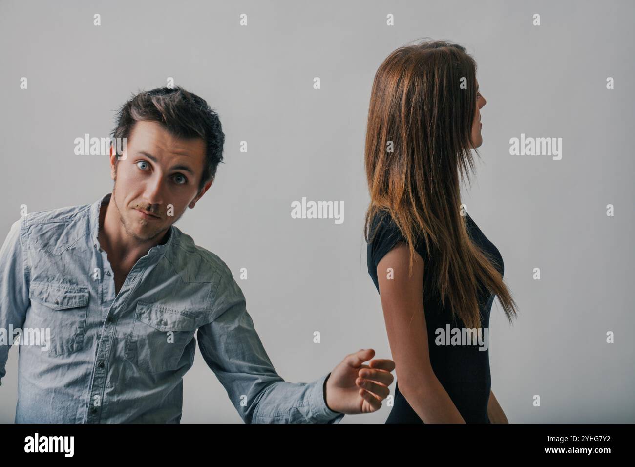 Der junge Mann greift auf eine Frau zu, die anscheinend beabsichtigt, sie zu umarmen. Sie wendet sich mit einem ernsten Ausdruck ab und ignoriert ihn pointiert. Er sieht überraschend aus Stockfoto