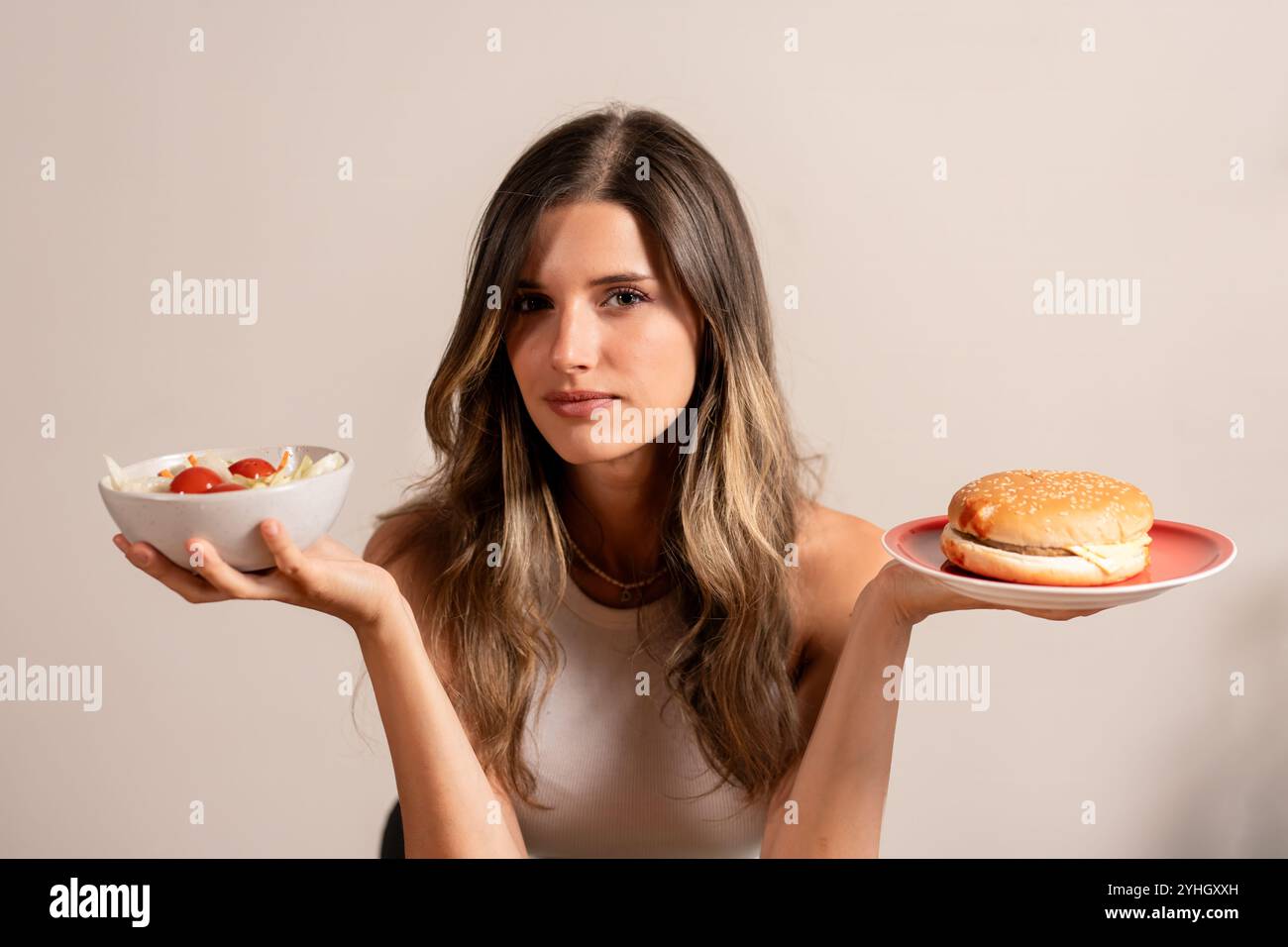 Junge Frau mit gesundem Salat und Hamburger, die das Dilemma bei der Auswahl von Lebensmitteln zeigt, gesunde versus ungesunde Ernährung Lebensstil Konzept Stockfoto