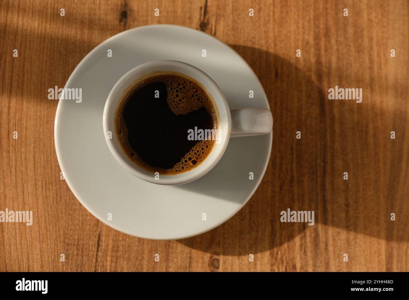 Eine dampfende Tasse Kaffee sitzt elegant auf einer hölzernen Oberfläche, die sich im sanften Licht des Morgenlichts sonnt. Stockfoto