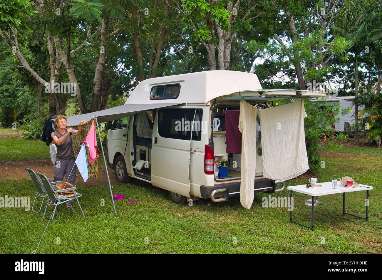 Frau hängt Wäsche zum Trocknen auf einem Campingplatz in der Nähe von Darwin, Northern Territory, Australien. Kleines Wohnmobil, Campingmöbel und tropische Vegetation Stockfoto