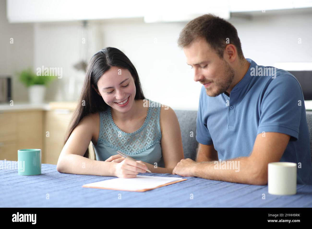 Glückliche Mitbewohner oder ein Paar, das einen Vertrag in der Küche zu Hause unterzeichnet Stockfoto