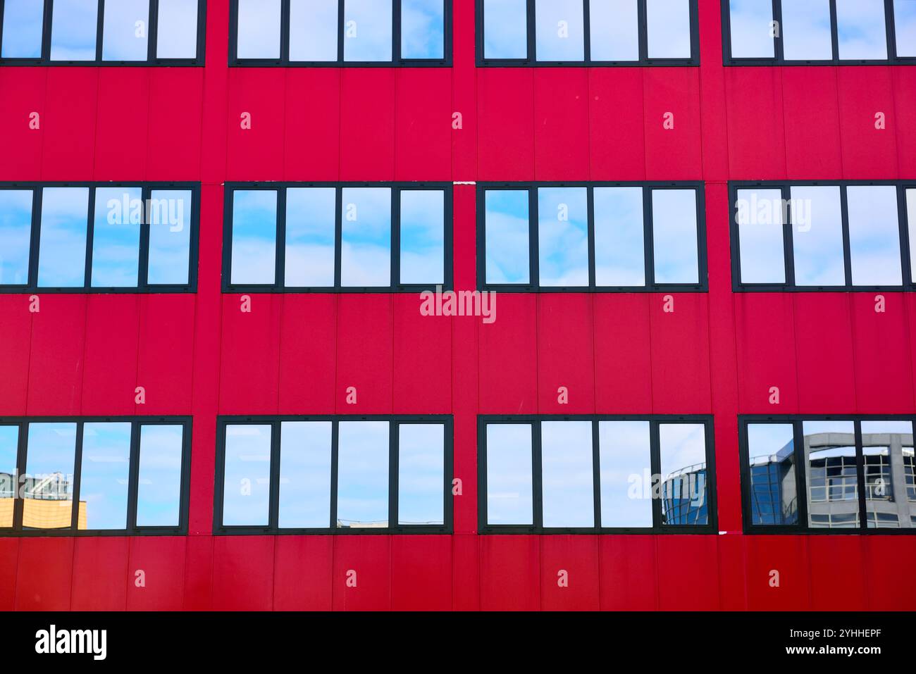 Dunkelrotes Gebäude mit mehreren Spiegelfenstern, Reflexionen von Himmel und Wolken Stockfoto