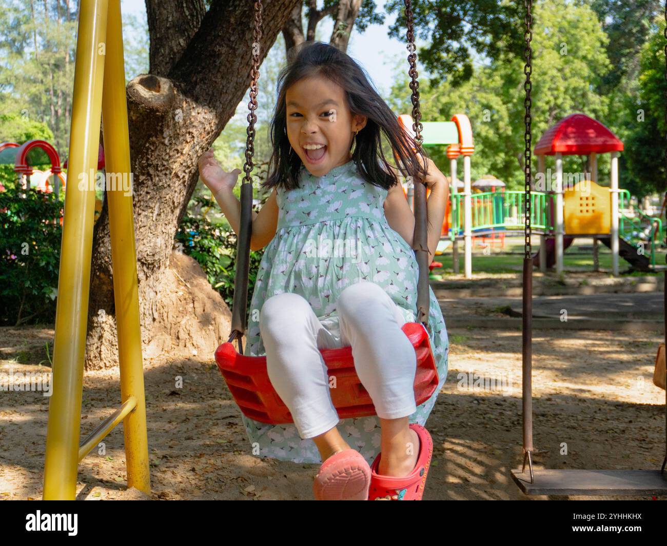 Süßes Mädchen, das Spaß auf der Schaukel auf dem Spielplatz im Park hat. Kinder spielen während der Sommerferien auf dem Spielplatz. Stockfoto