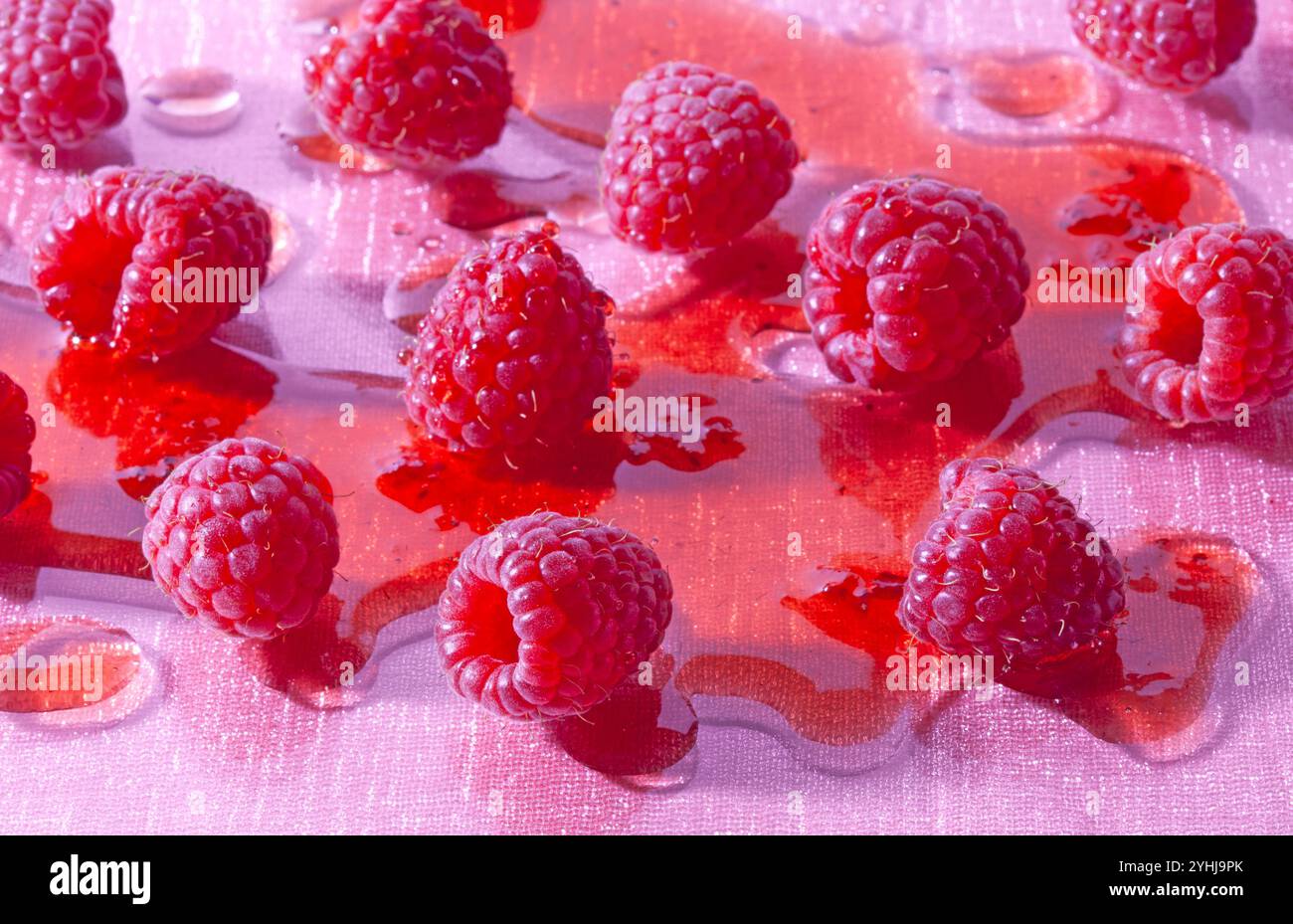 Himbeeren in Himbeersirup liegen auf einem rosafarbenen Glastisch. Stockfoto