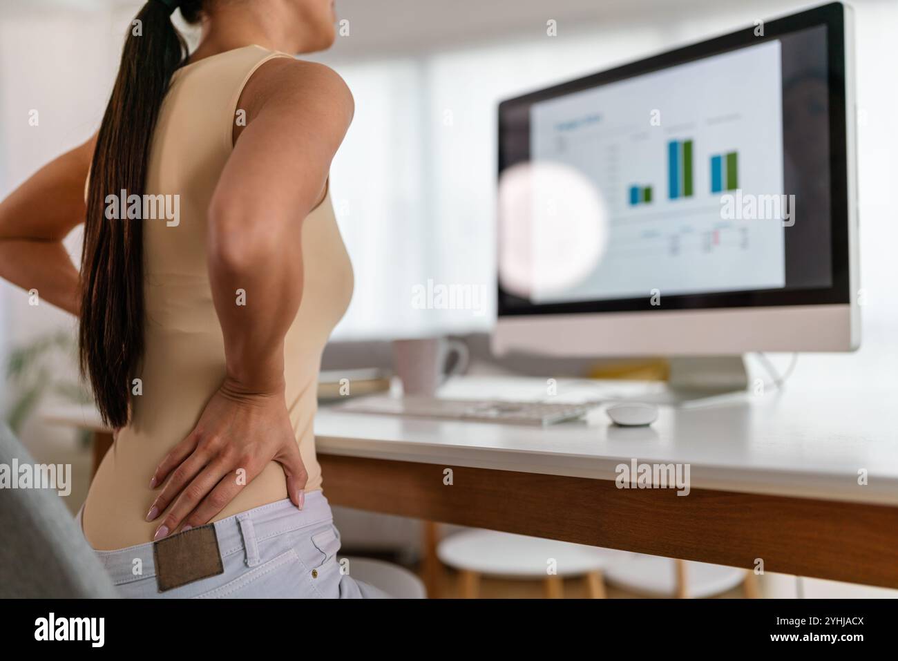 Müde Arbeitnehmerin sitzt am Schreibtisch, Rückenschmerzen leiden, Frau starke Rückenschmerzen, falsche Haltung Stockfoto