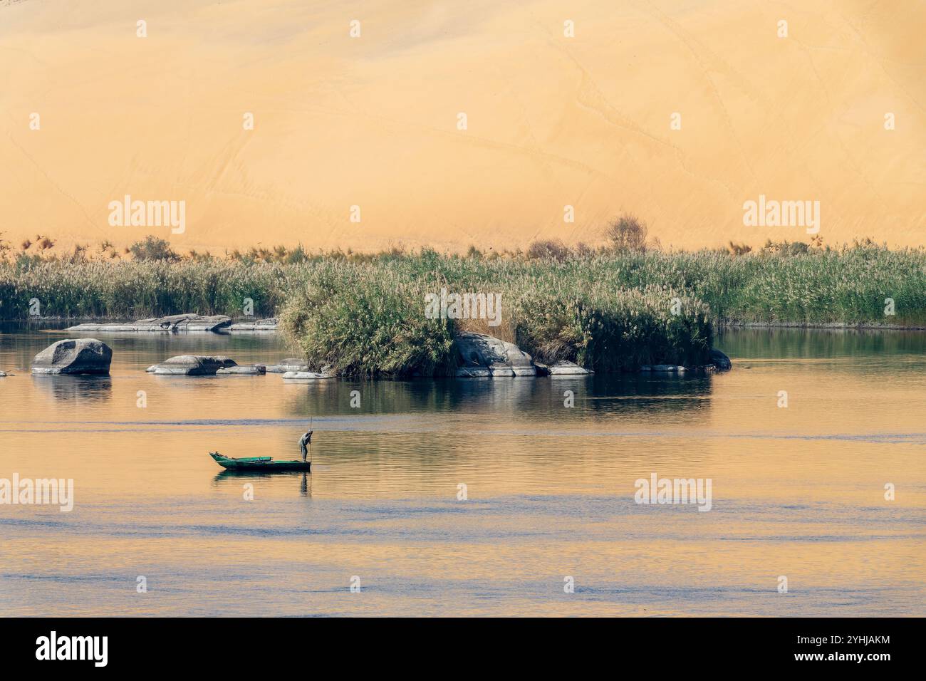 Fischer in einem Ruderboot auf dem Nil bei Sonnenuntergang, malerische Landschaft mit Felsen im Wasser und Sanddünen-Reflexionen in Assuan, Ägypten Stockfoto