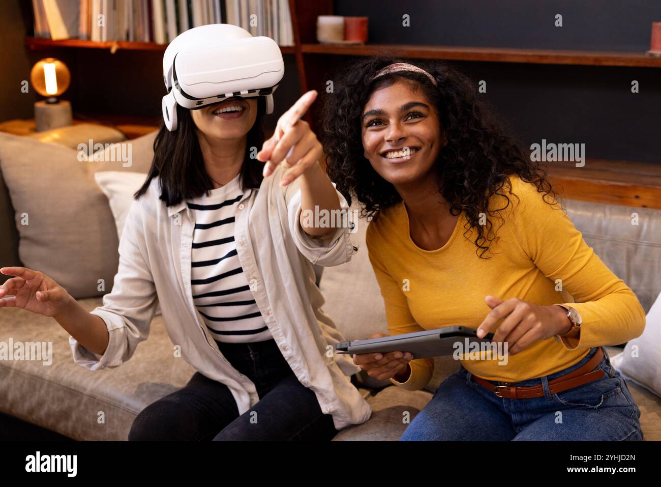 Zu Hause, Freunde, die ein Virtual-Reality-Headset verwenden, lächeln und zeigen aufgeregt Stockfoto